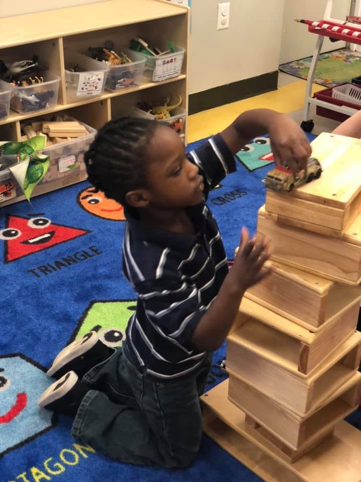 Child playing with a toy car on a stack of wooden blocks