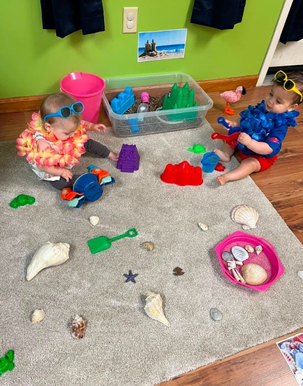 Two children playing with beach toys and seashells on a rug