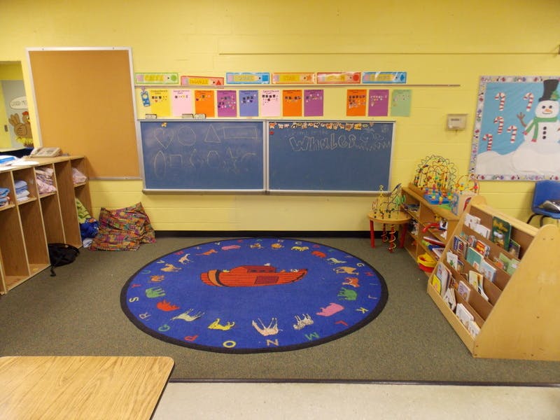 Classroom with a blue circular rug, chalkboards, and shelves