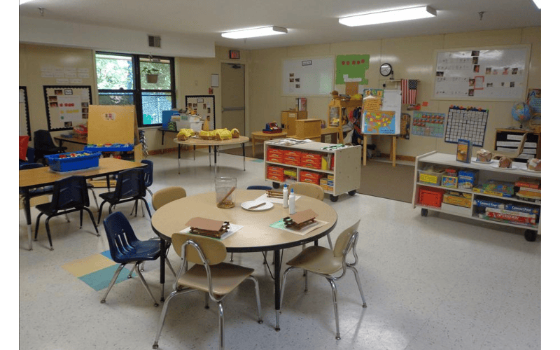 An empty classroom with small tables and chairs, and learning materials