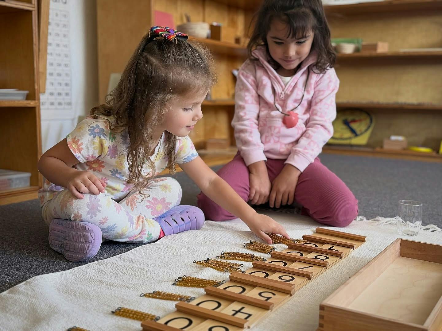Two children sitting on the floor using a Montessori bead and number activity
