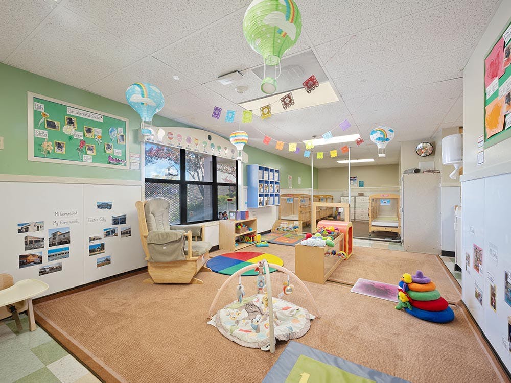 A childcare center playroom with cribs, rocker, playmats, and toys