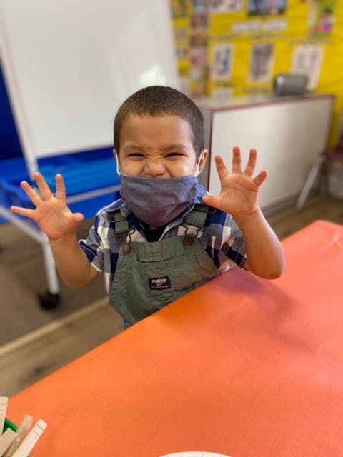 Child in a mask making a face and holding up hands