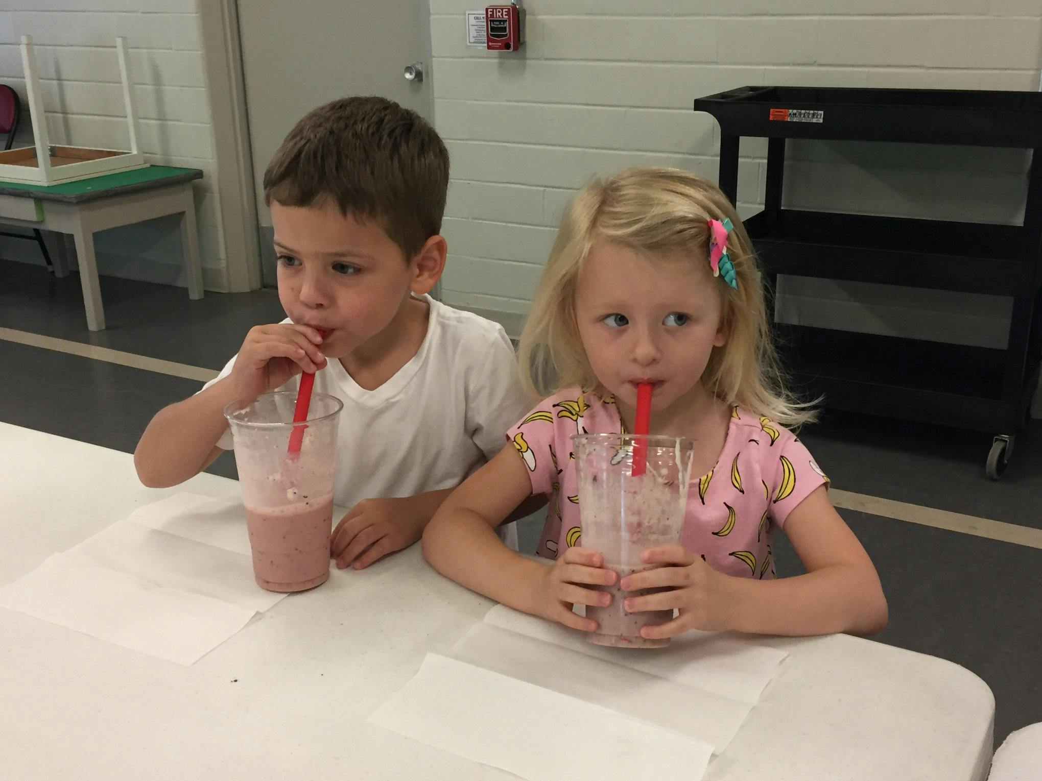 Two children drinking from cups with straws