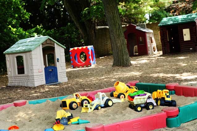 Sandbox with toy trucks and playhouses in a yard
