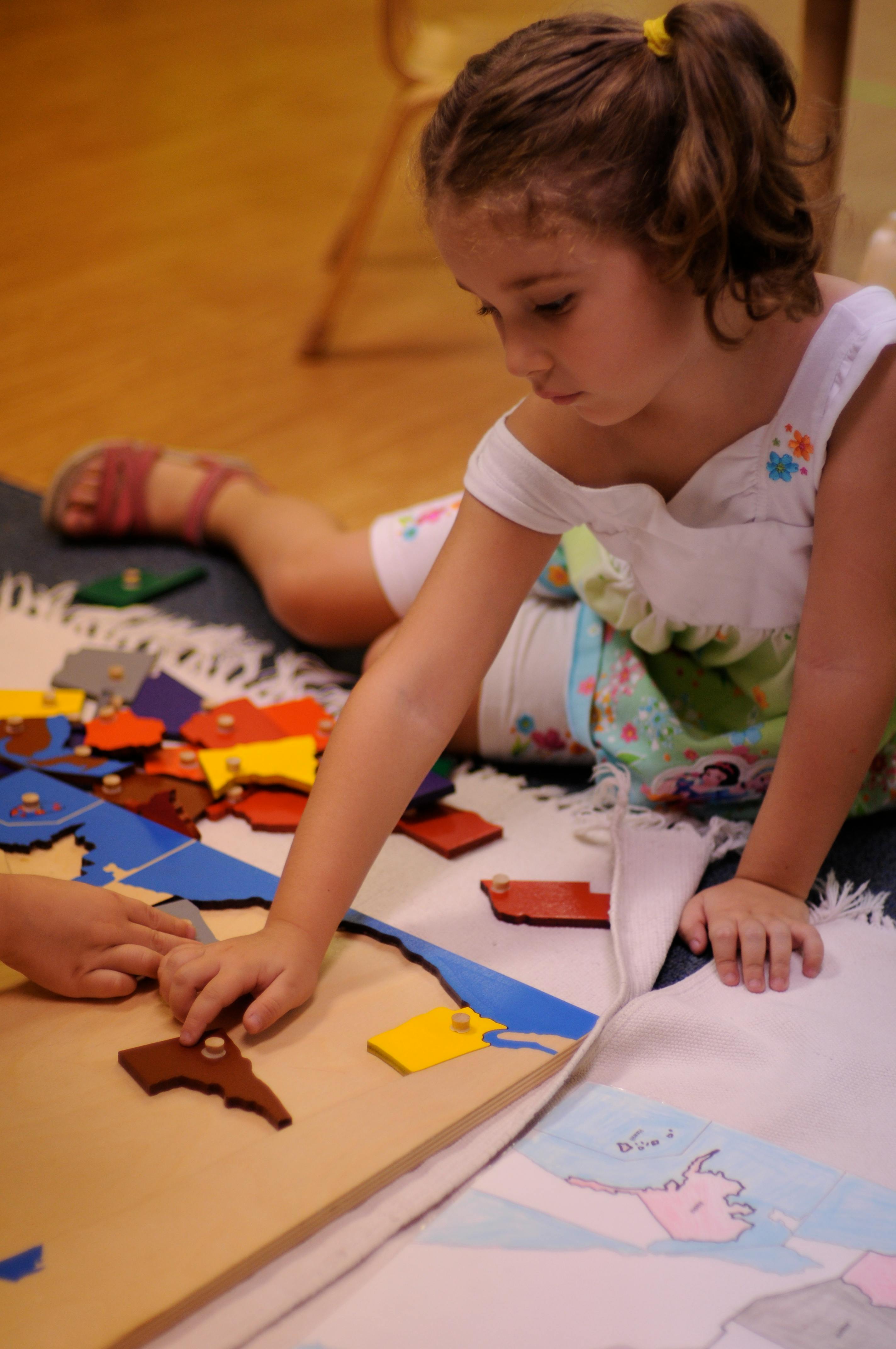 Child playing with a wooden puzzle map on the floor
