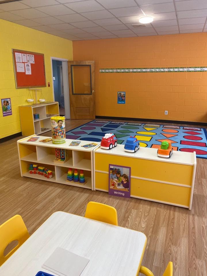 Classroom with colorful rug, shelves of toys, and small table with chairs
