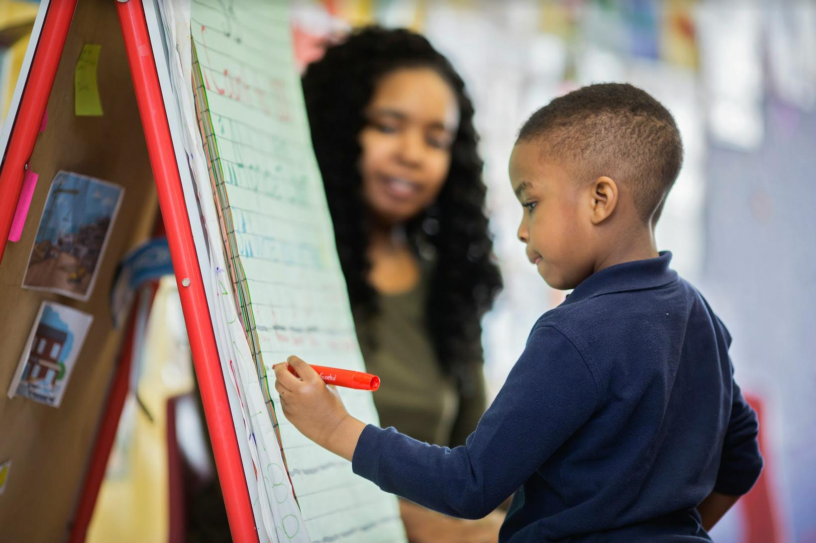 Child writing on an easel with a person in the background