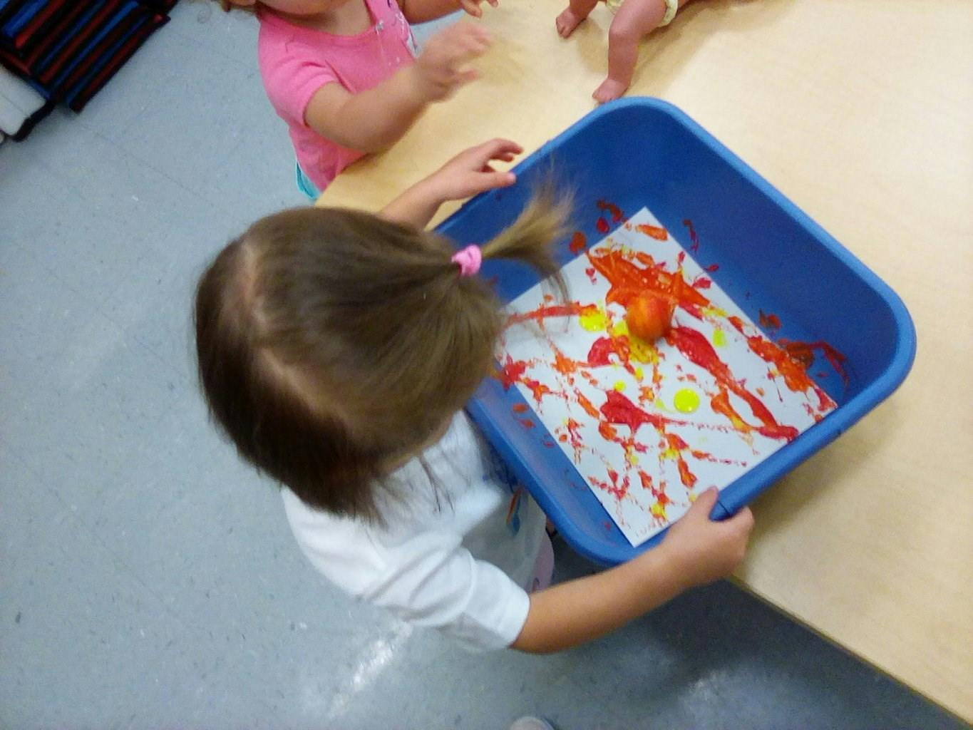 Child holding a blue bin with paper and paint