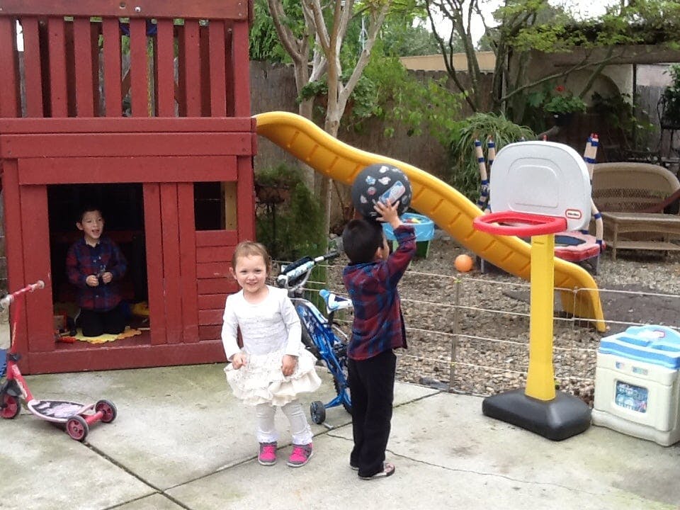 Three children playing on a playground with a slide and basketball hoop