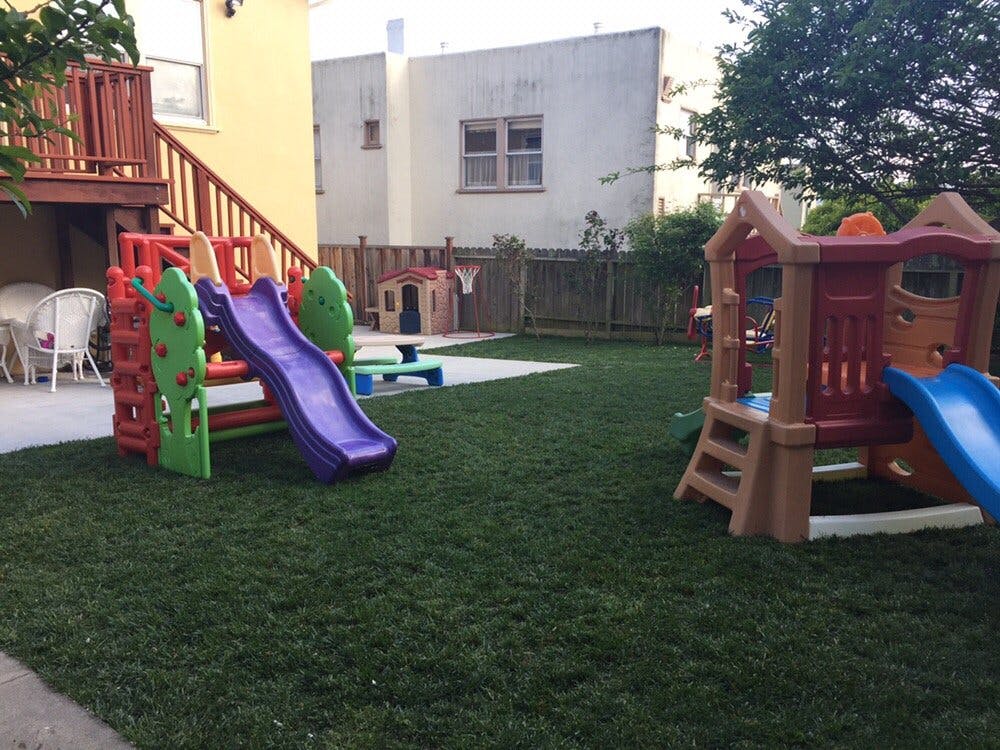 Two colorful plastic play structures with slides on a grassy lawn