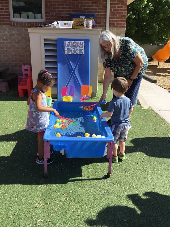 Adult and two children playing with a water table outdoors