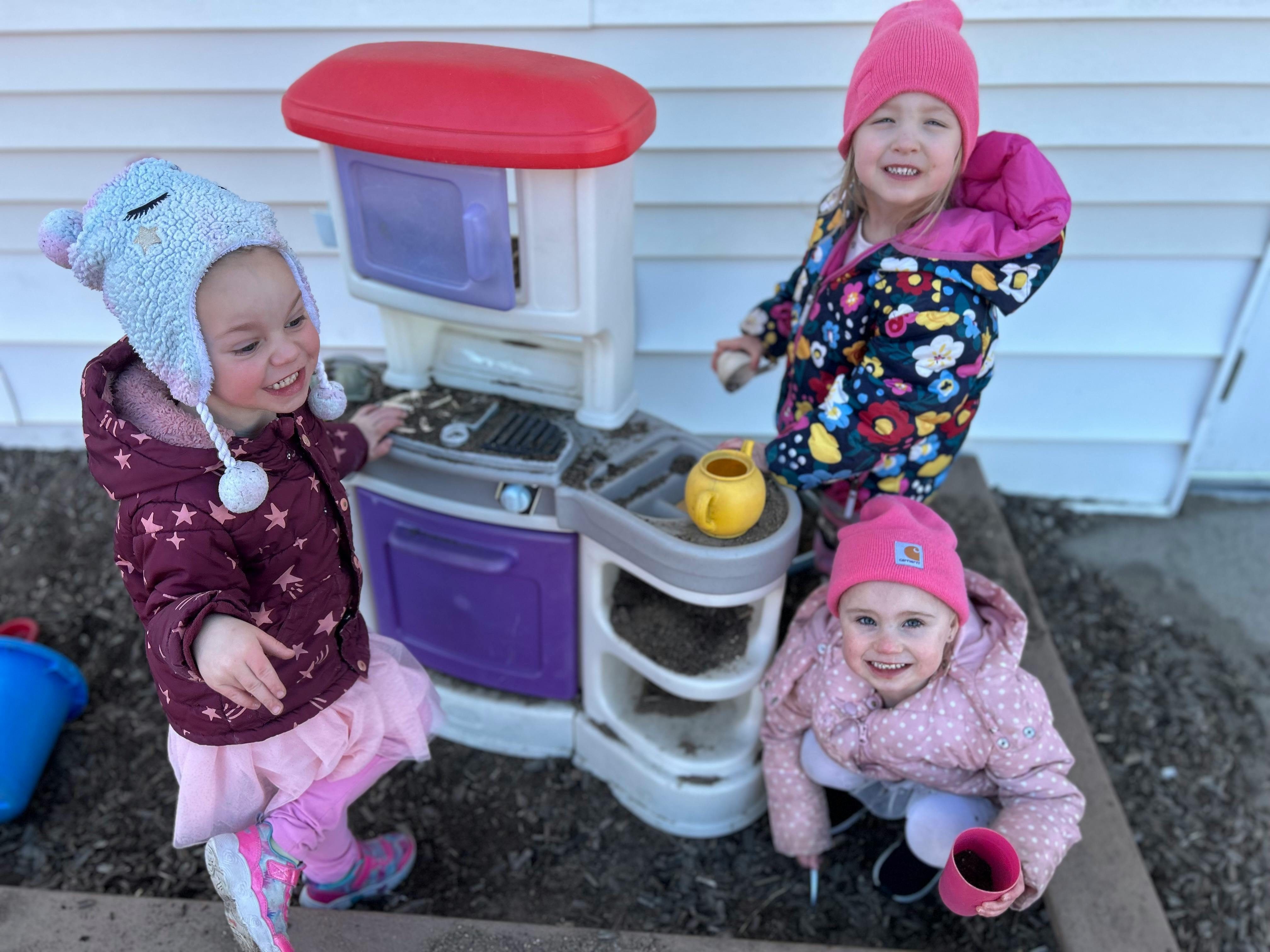 Three children playing with a toy kitchen outdoors