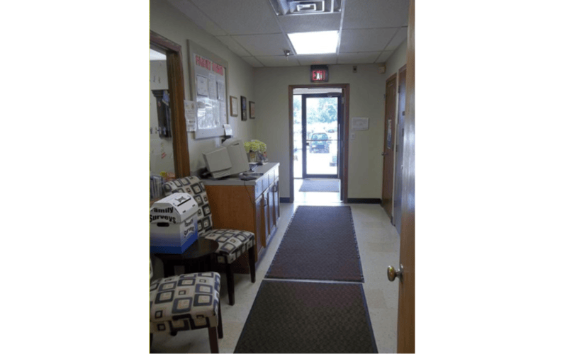 A hallway with chairs, a counter with a computer, and an open door at the end