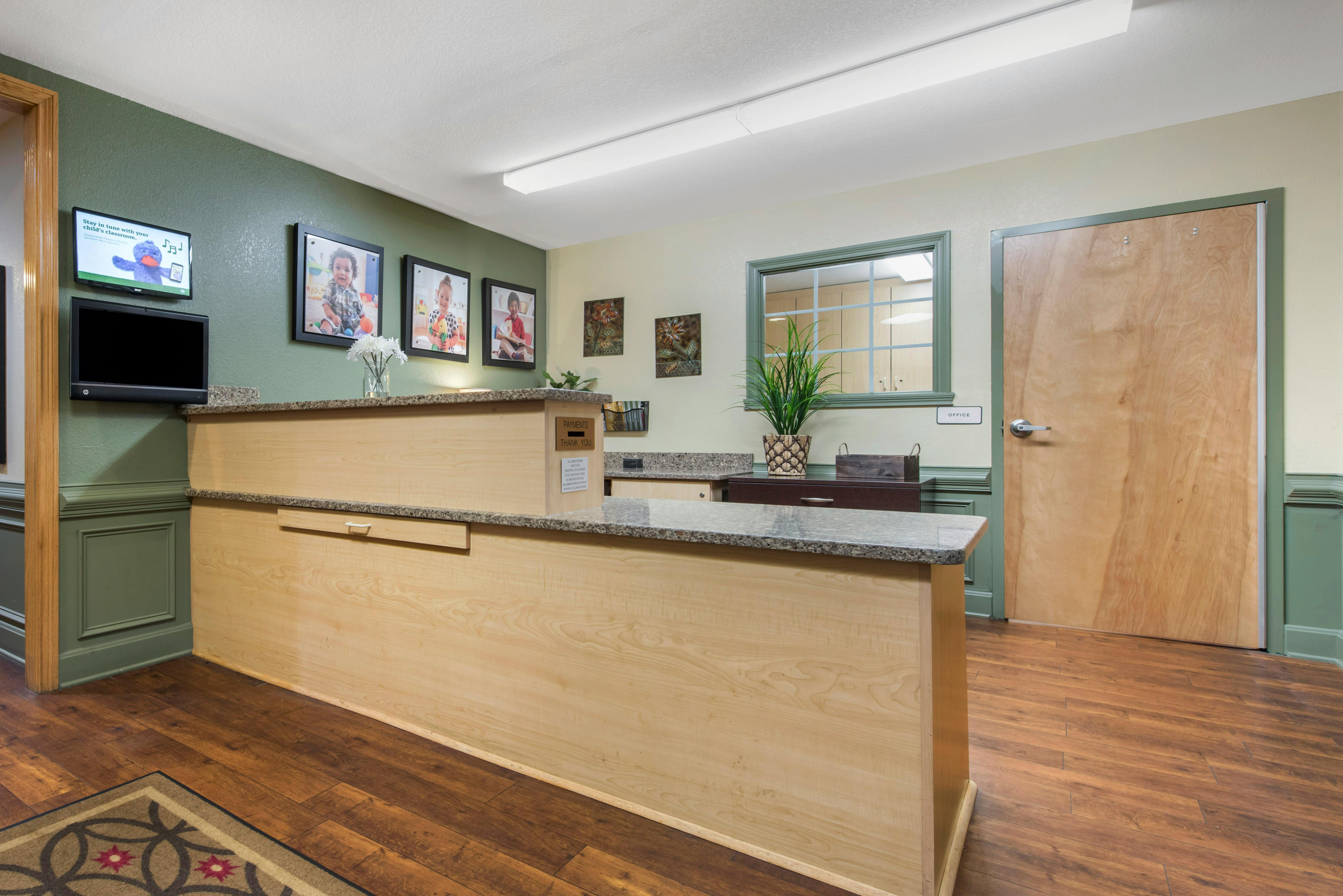Wood and granite reception desk with monitors, framed photos, and a potted plant