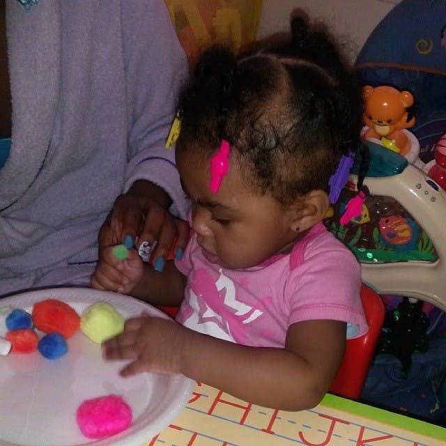 Child playing with colorful pom-poms on a white plate