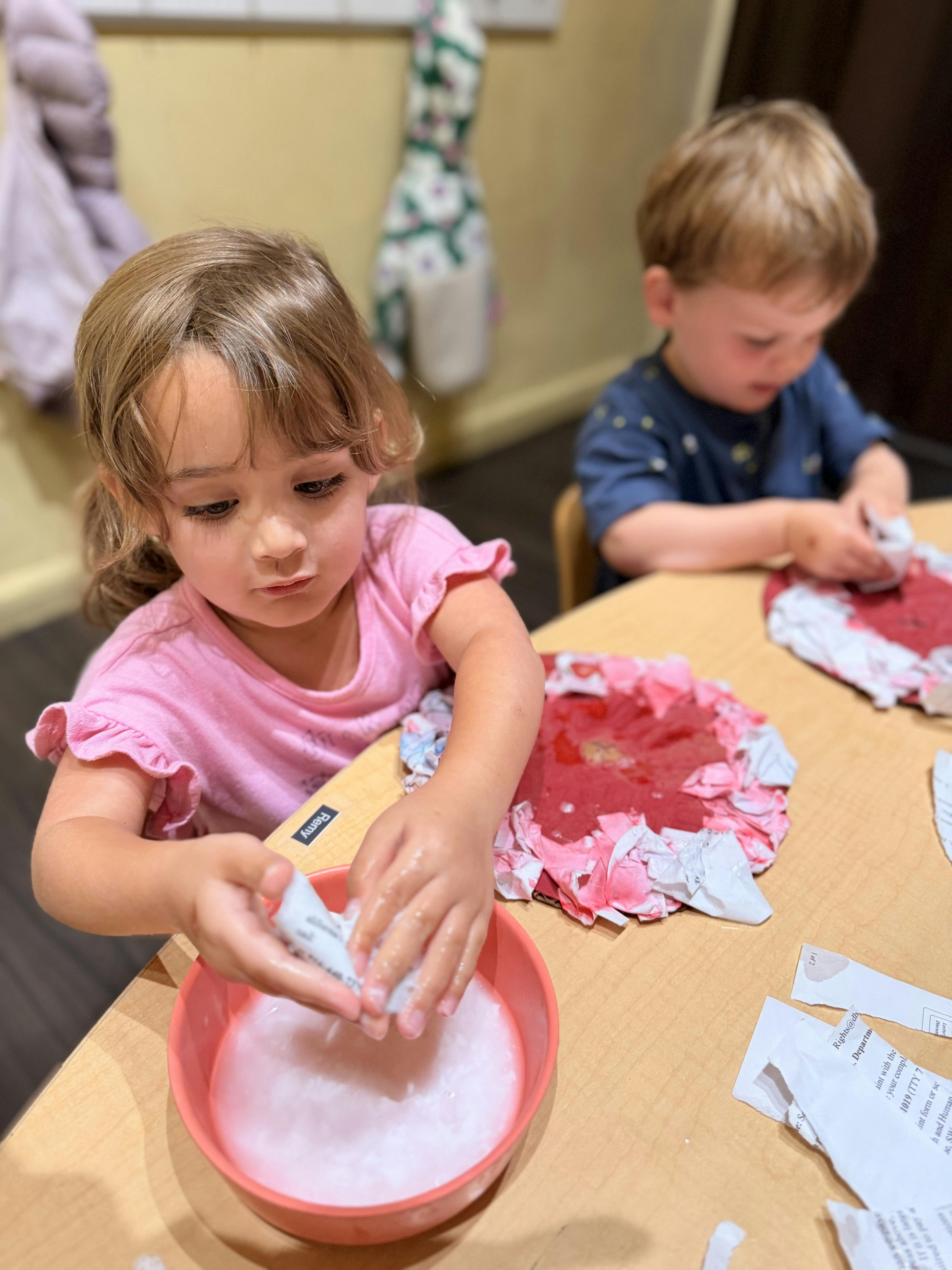 Two children sitting at a table crafting with paper and liquid