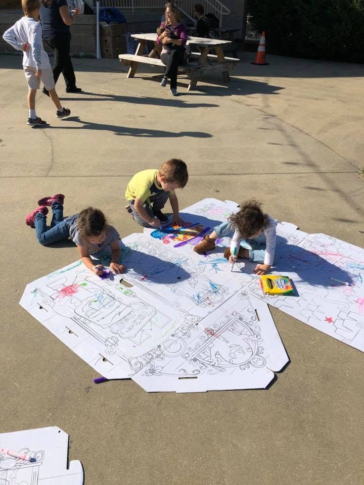 Three children coloring on large sheets of paper on the ground