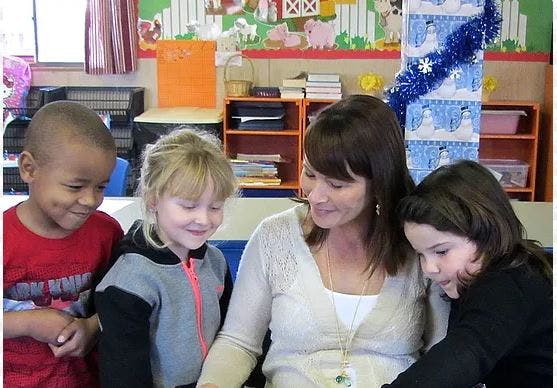 Adult and three children looking down in a classroom