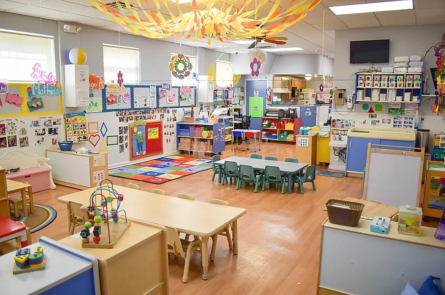 A colorful classroom with small tables and chairs, toys, and decorations