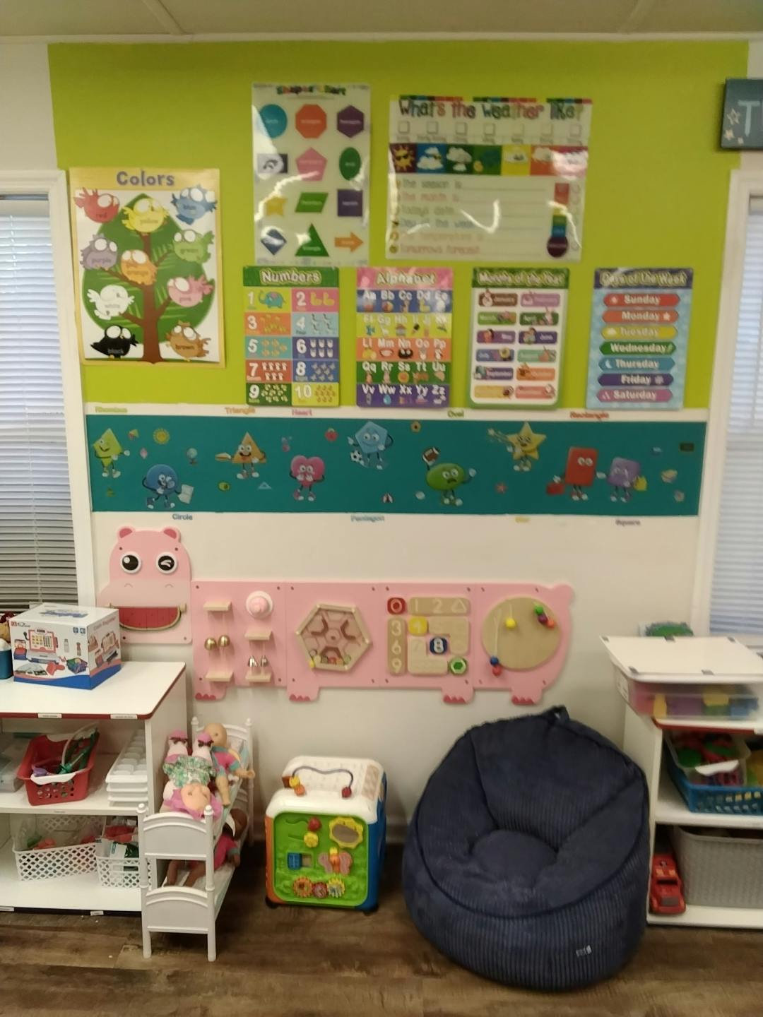 Classroom wall with educational posters, a pink activity board, and toys