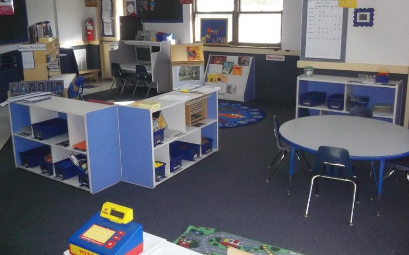 Classroom with tables, chairs, shelving units, and a word wall