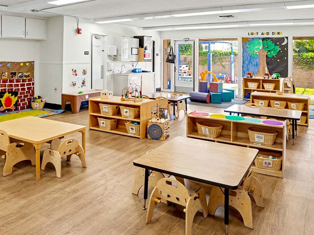 Empty children's classroom with small tables and chairs, toys, and an outdoor area