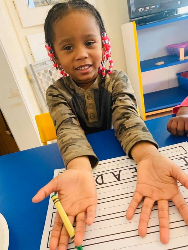 Child with braided hair and beads holding a crayon over a worksheet