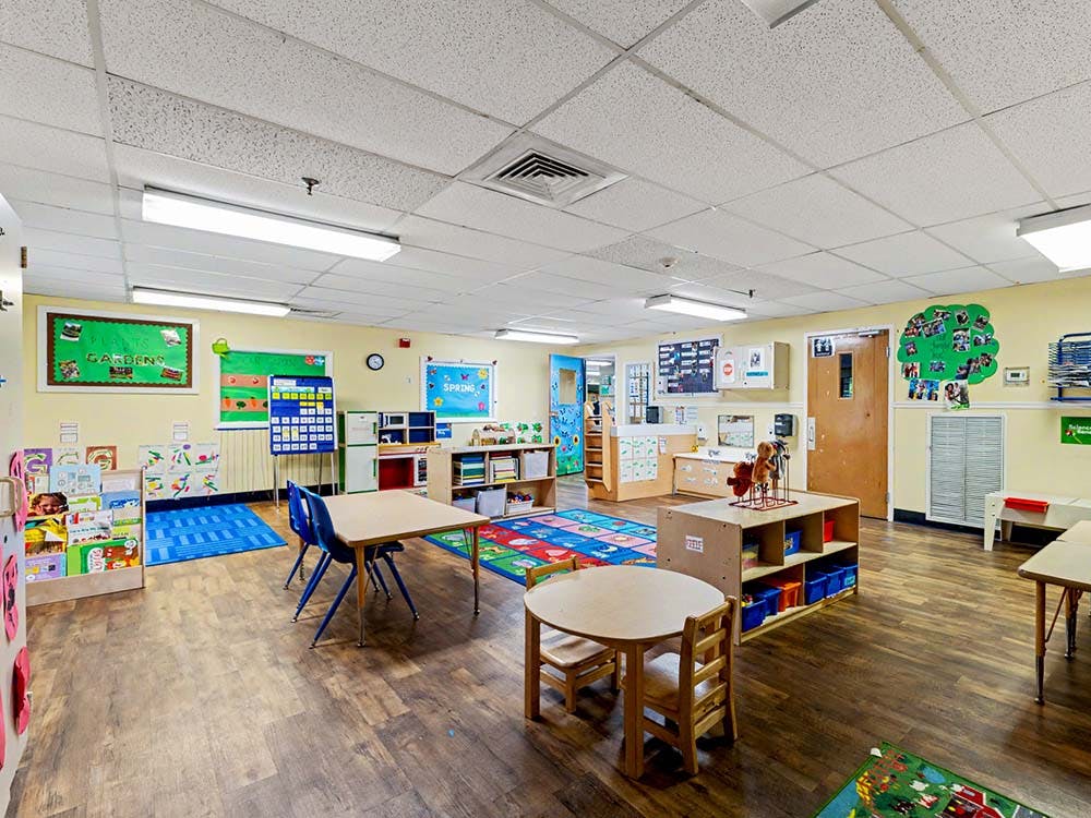 Classroom with small tables, chairs, colorful rugs, and learning materials