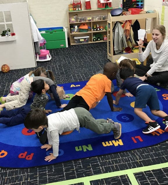 Children doing push-ups on a blue rug with a person observing them