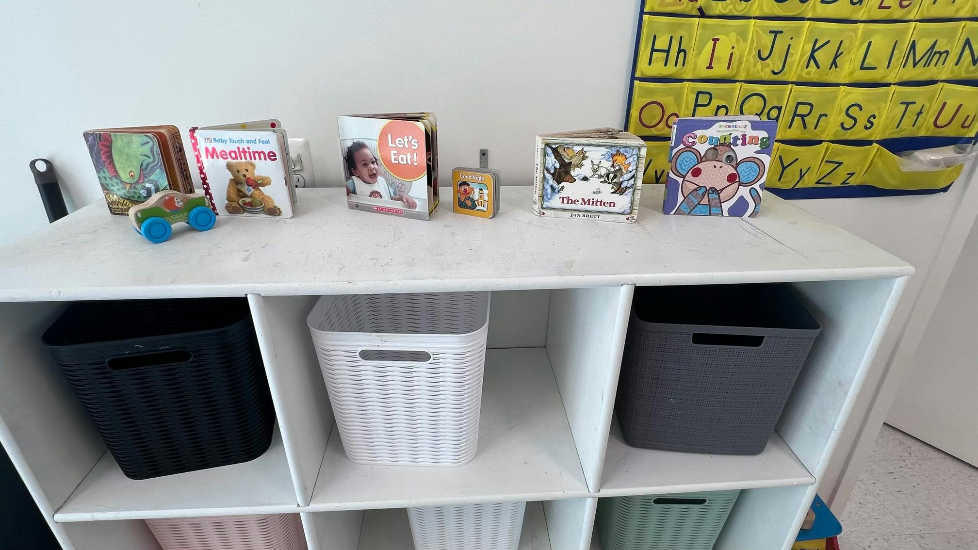 Childrens books and a toy car on a shelf with storage bins