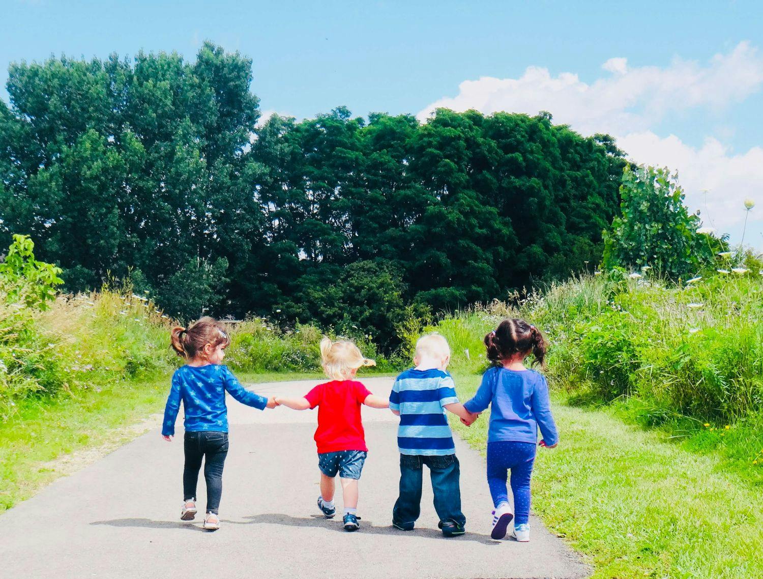 Four children holding hands walking on a path