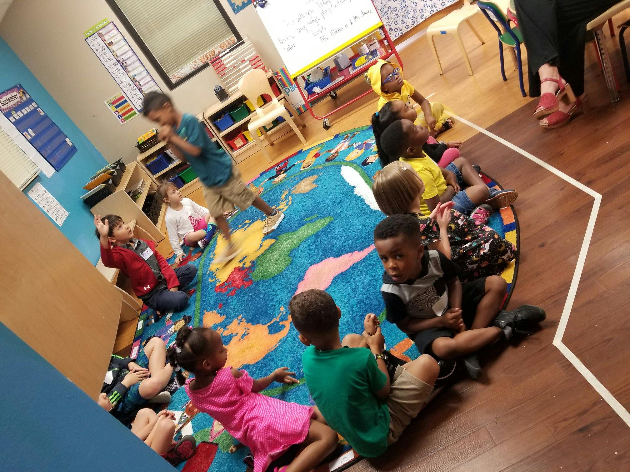 Children sitting on a world map rug in a classroom