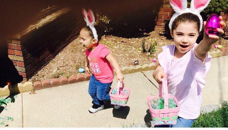 Two children wearing bunny ears and holding baskets, one holding up an egg