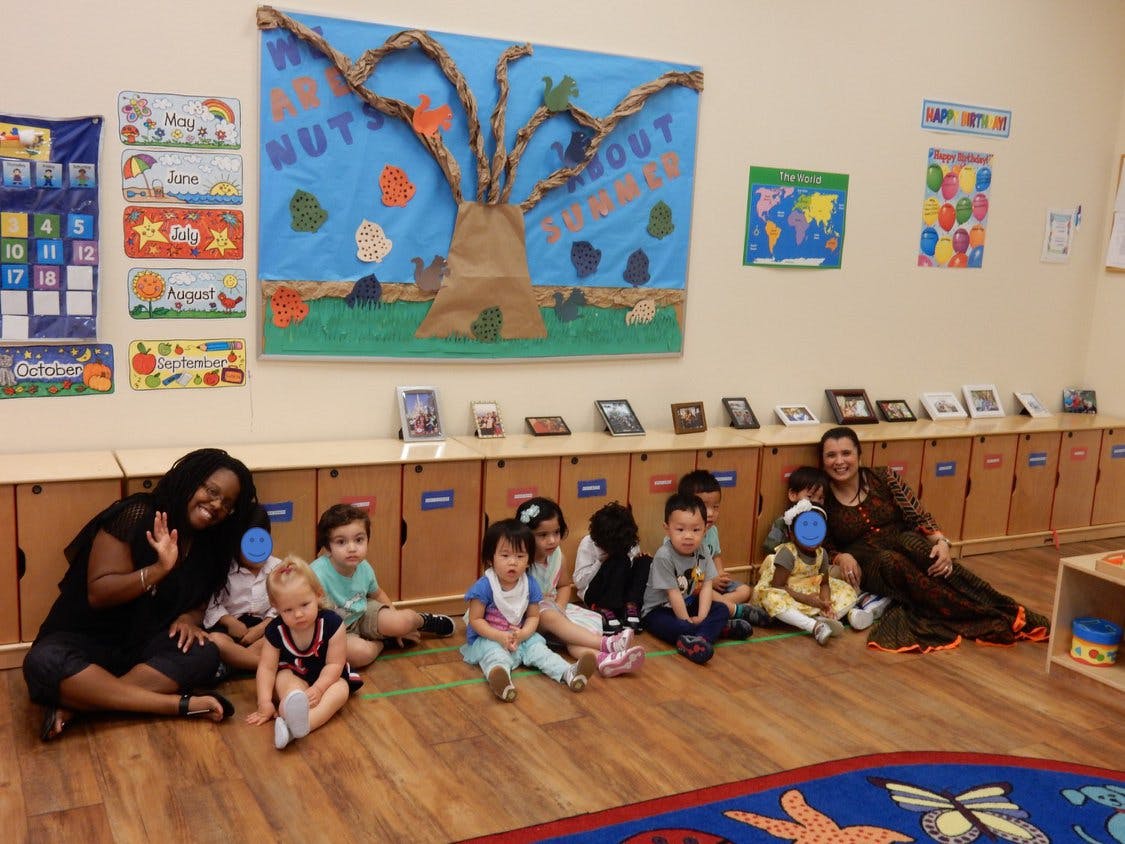 Two adults and multiple children sitting on a wooden floor in a classroom