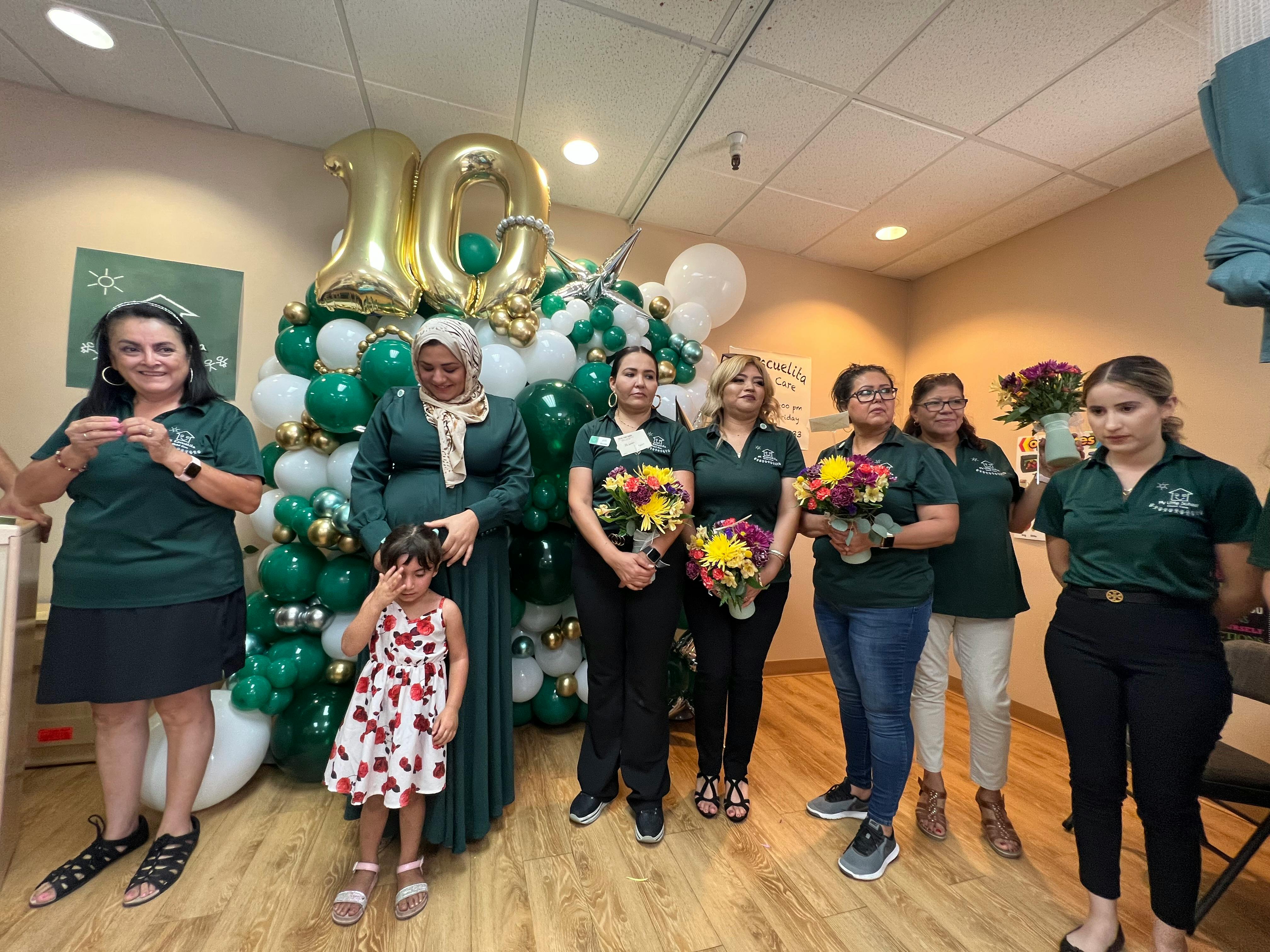 Group of people holding flowers in front of a balloon display with the number 10