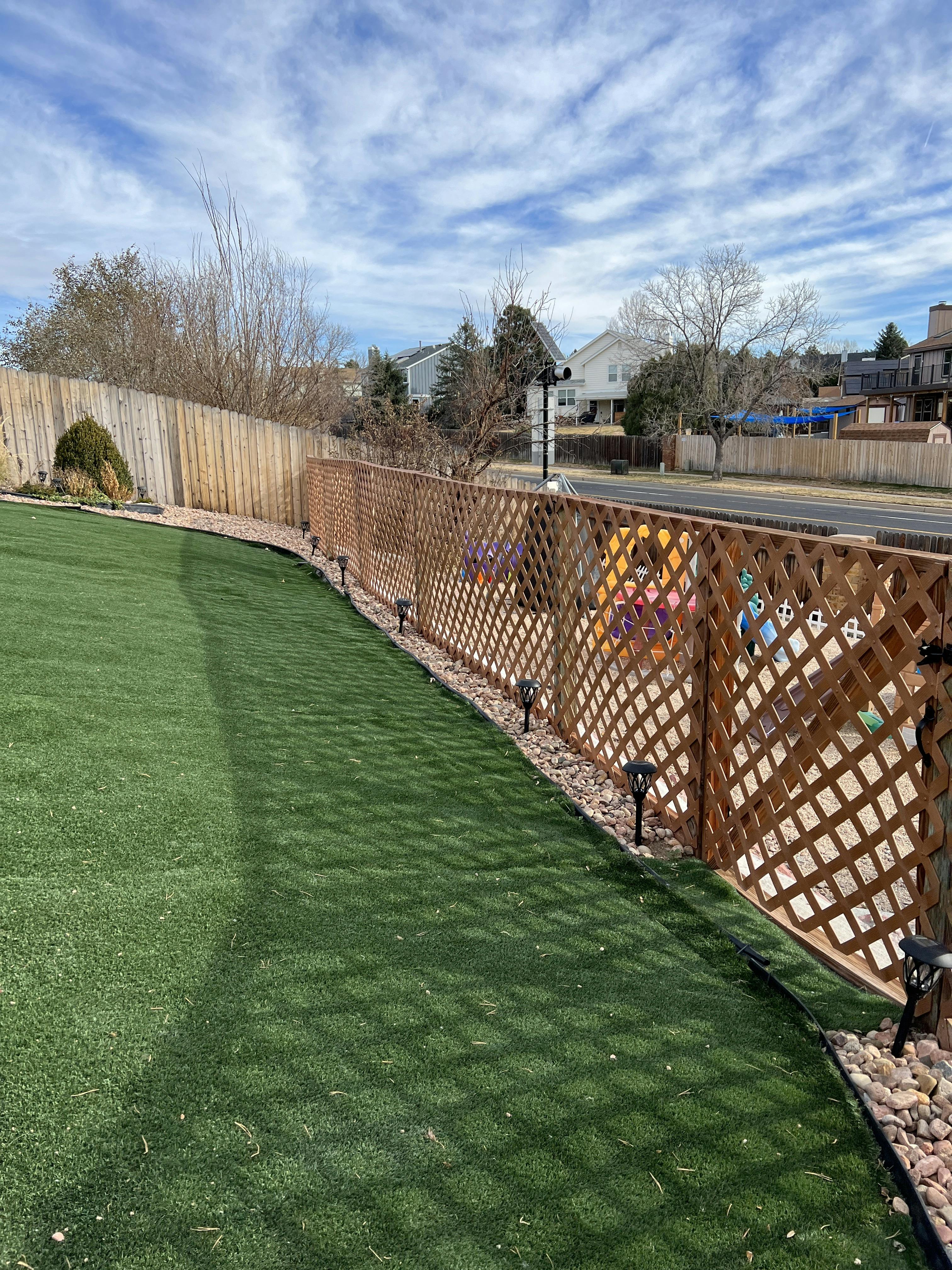 An artificial turf lawn next to a wooden fence and decorative lattice with yard lights