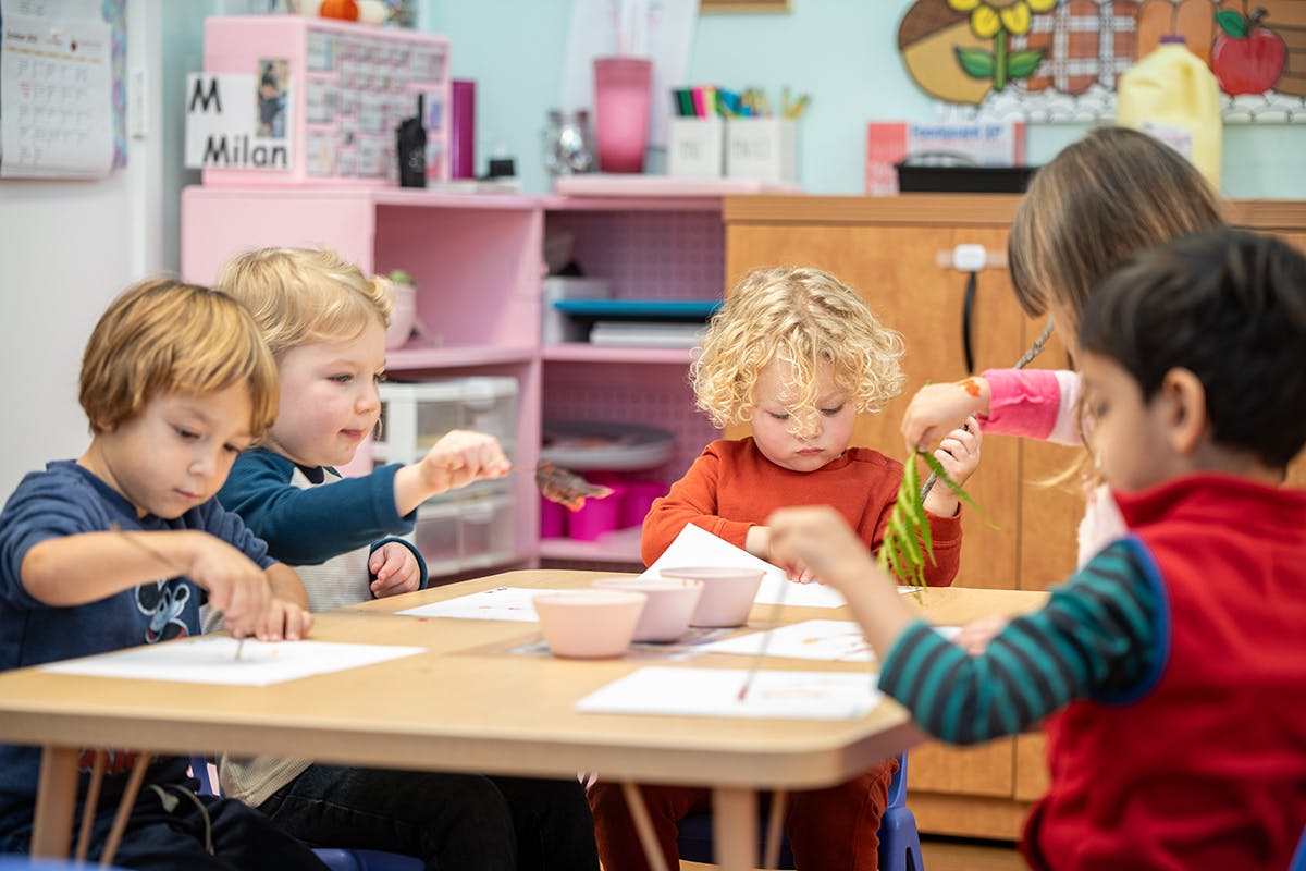 Children at a table drawing and playing with leaves in a classroom