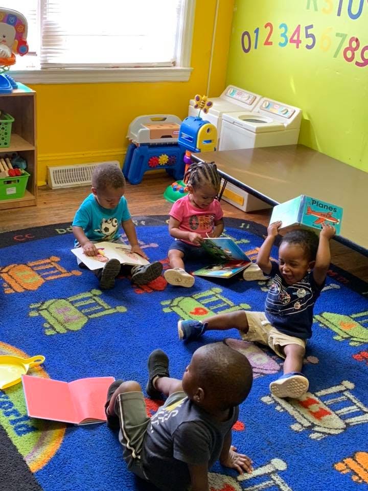 Four children sitting on a rug, reading books in a classroom