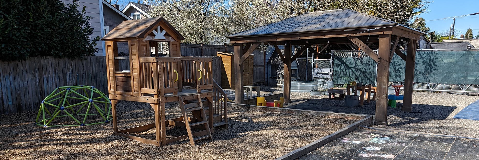 Outdoor playground with a wooden playhouse, a geodesic dome, and a covered sandbox area