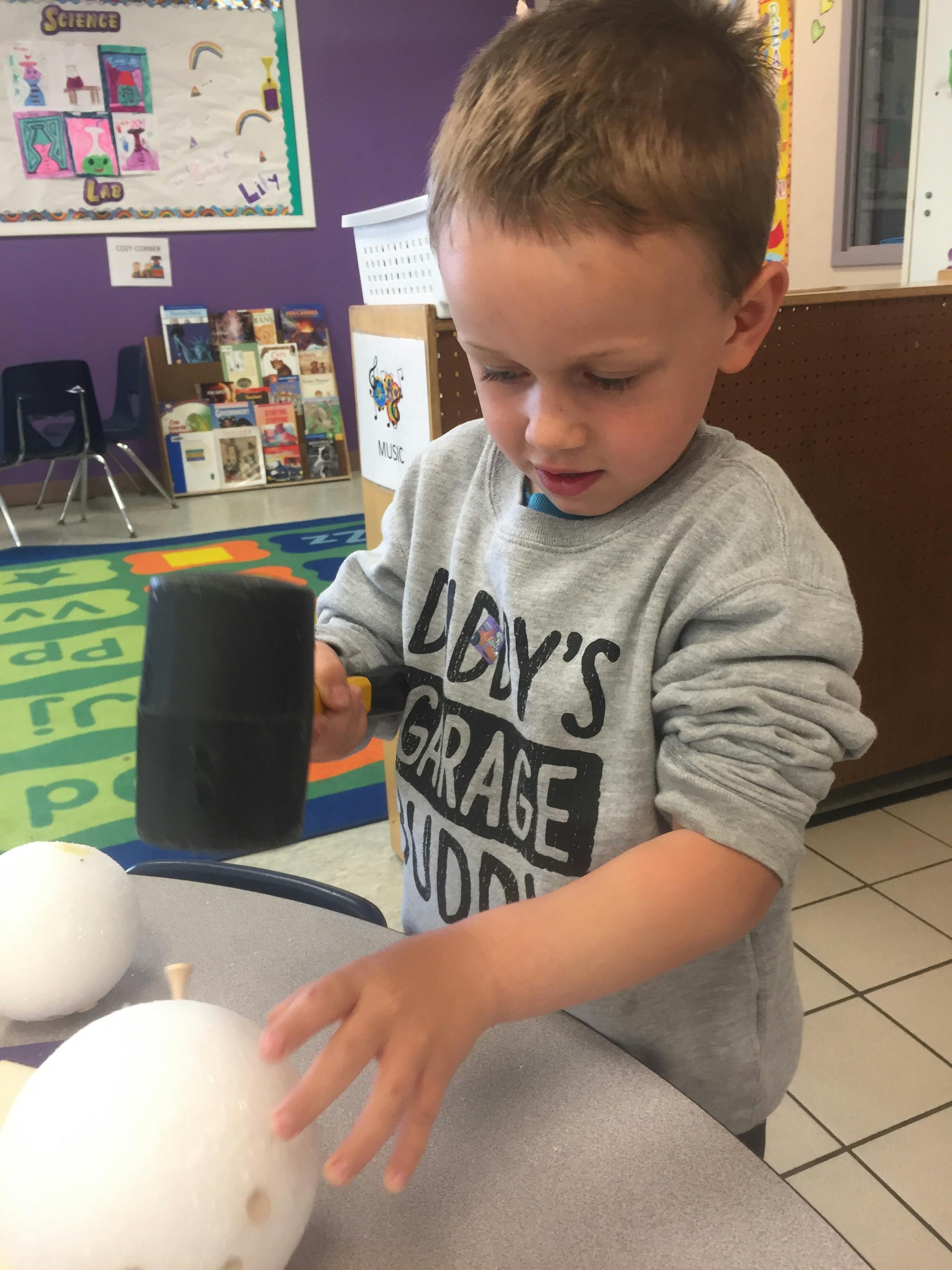 Child holding a mallet over a white sphere with holes object