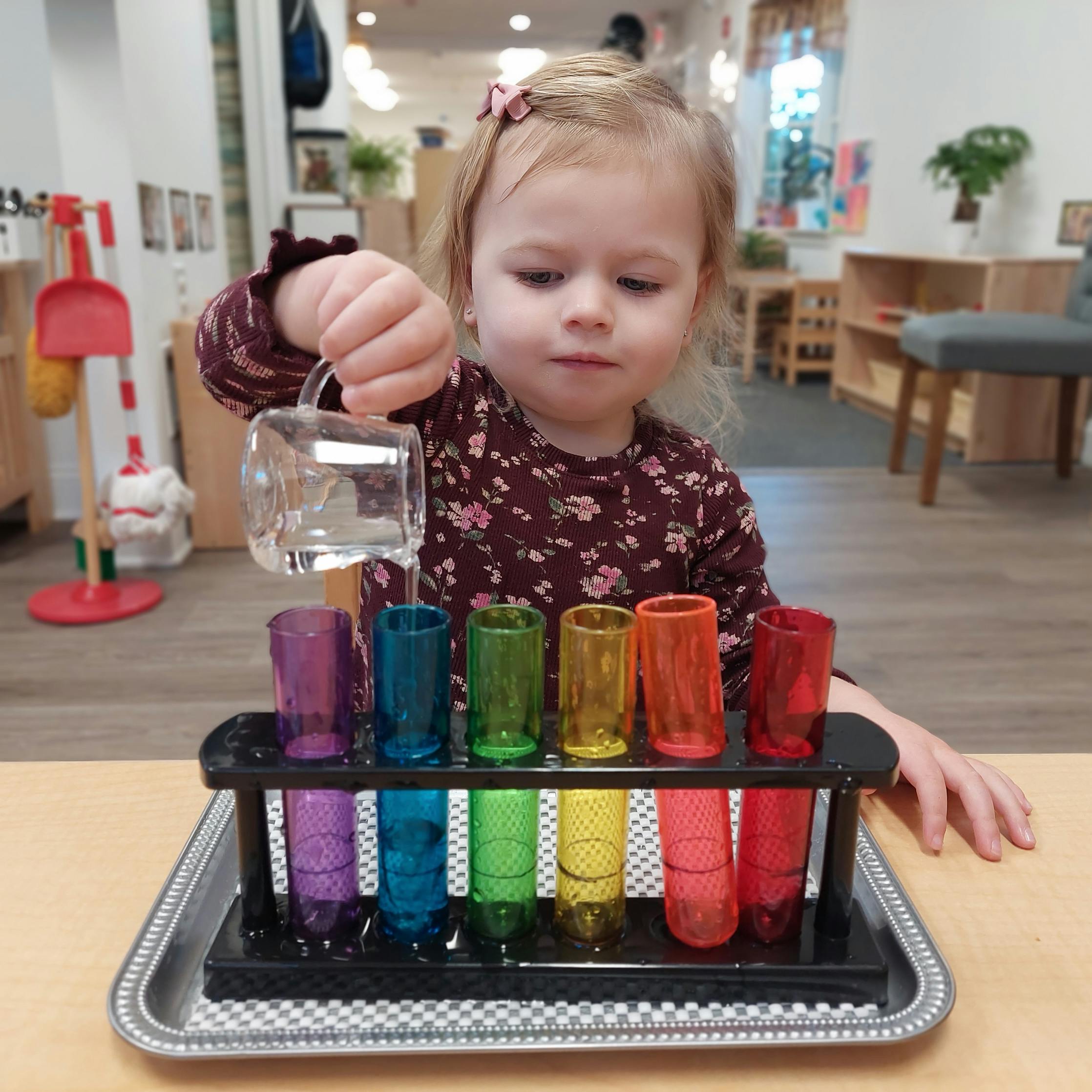 Child pouring water from a small pitcher into colorful test tubes