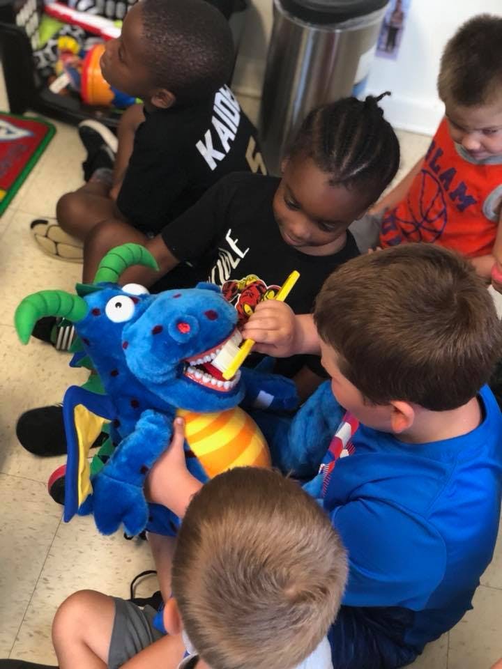 Children brushing the teeth of a dragon plush toy