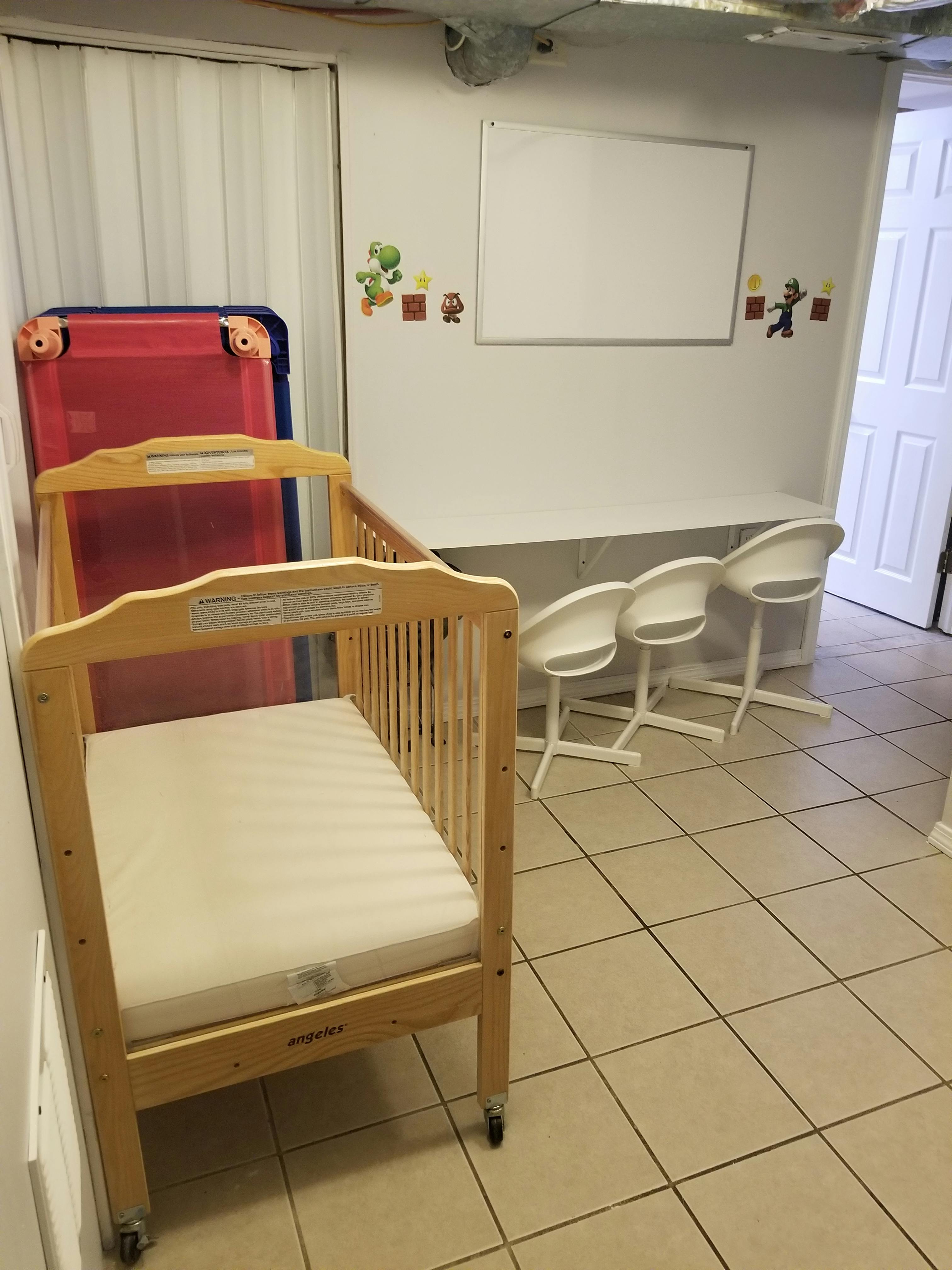 Wooden crib with a mattress next to a red and blue playpen