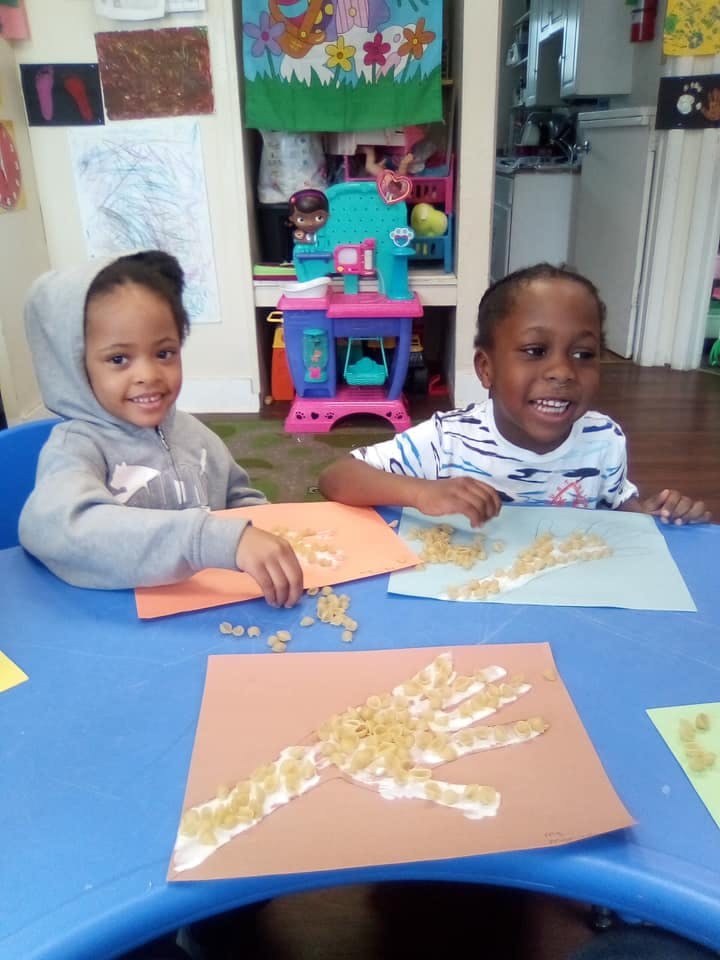 Two children making art with pasta on paper