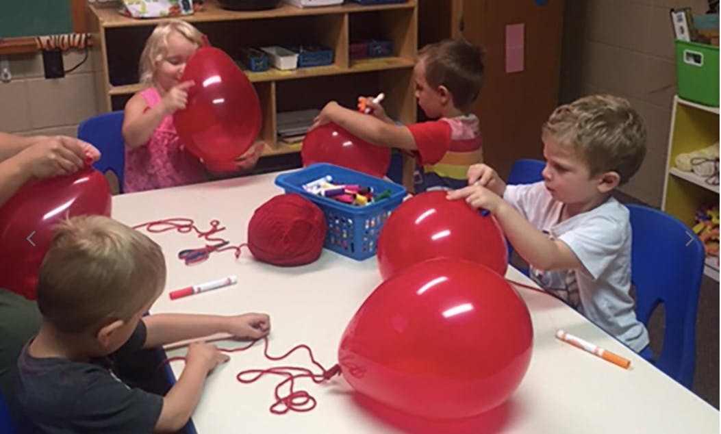 Children at a table with red balloons and string