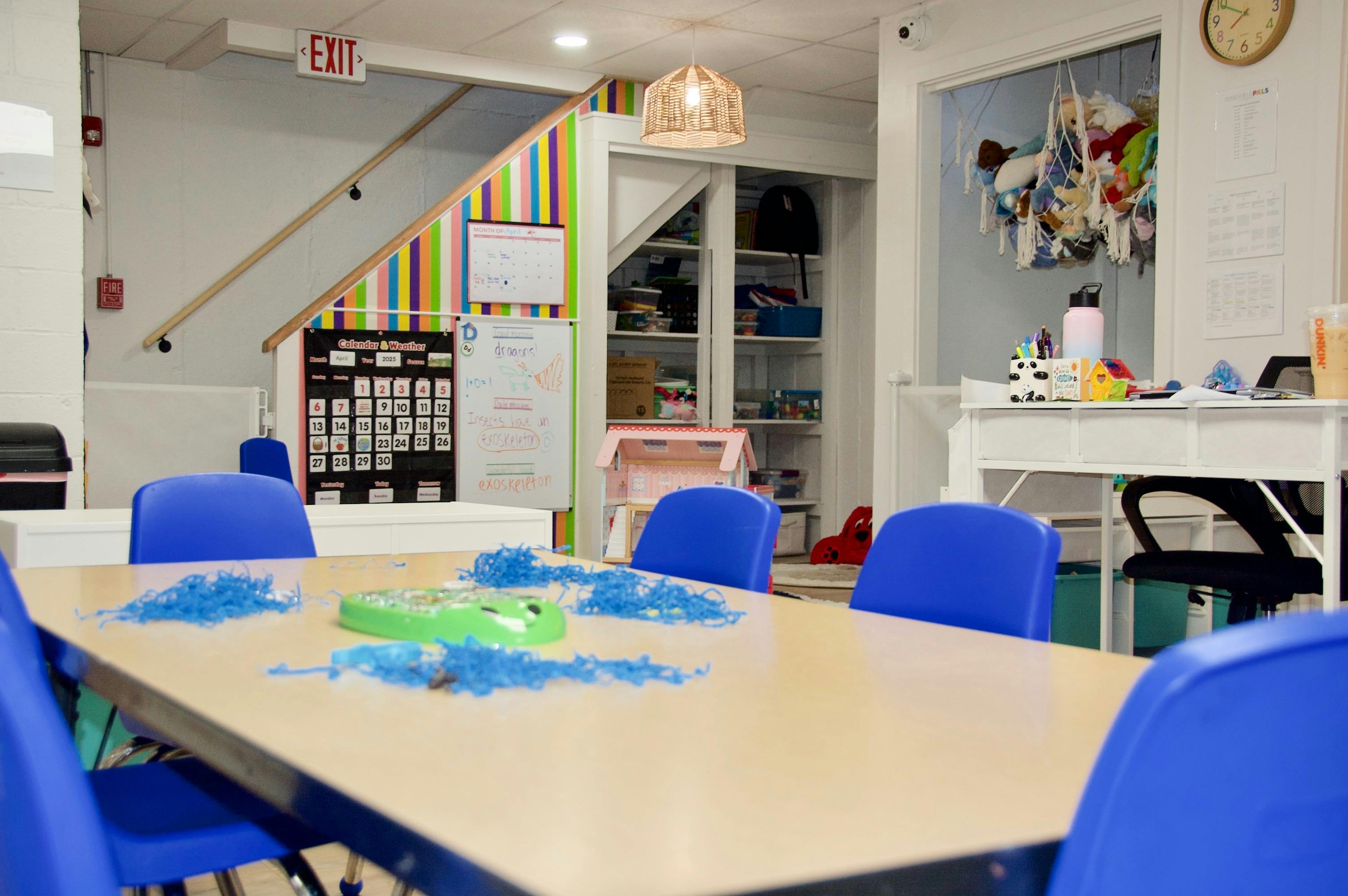 Classroom with blue chairs around a table with blue shredded paper, a whiteboard, and a calendar