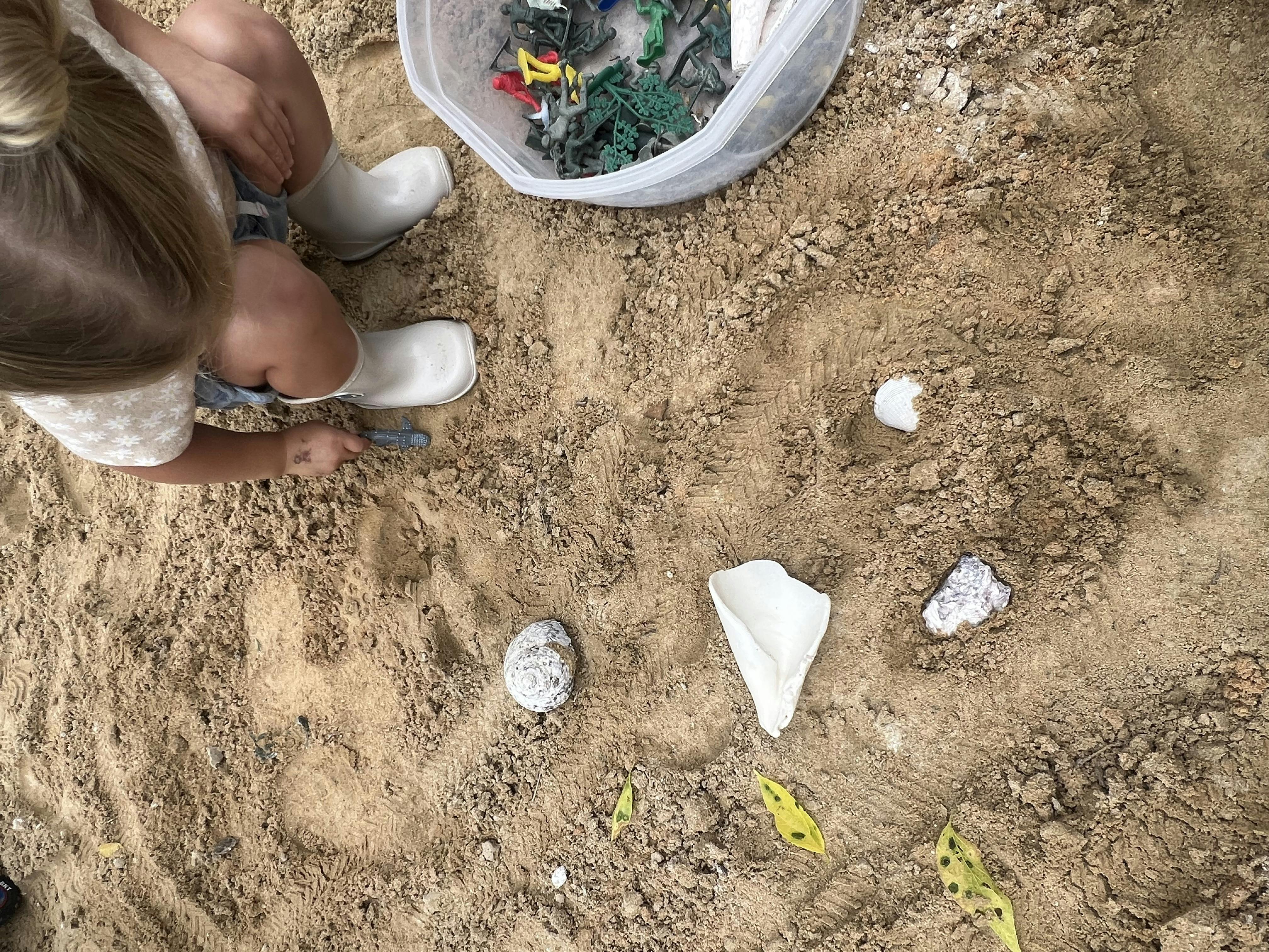 Child playing in sand with toy measuring tool and military figurines