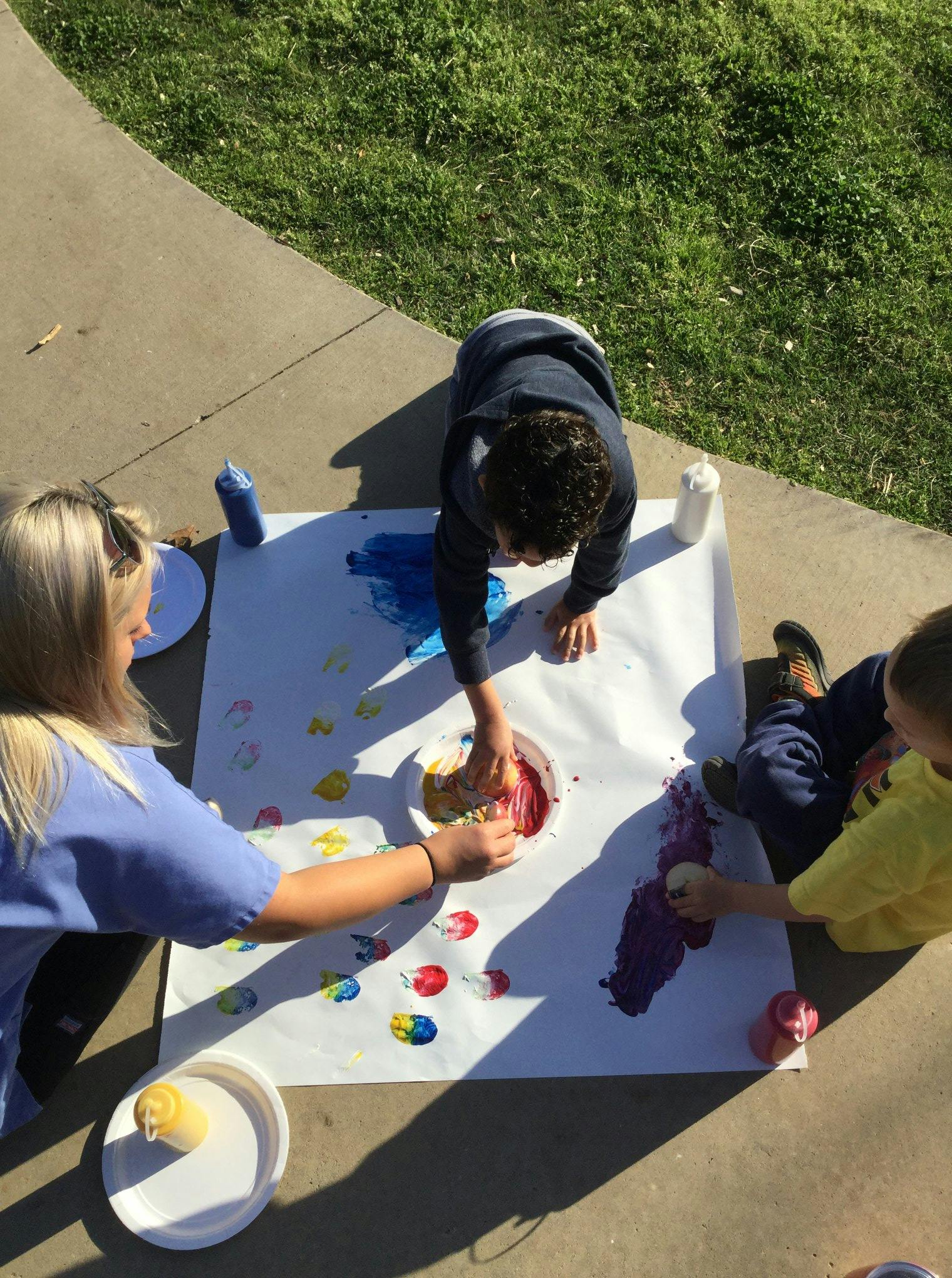 People finger painting on a large sheet of paper outdoors