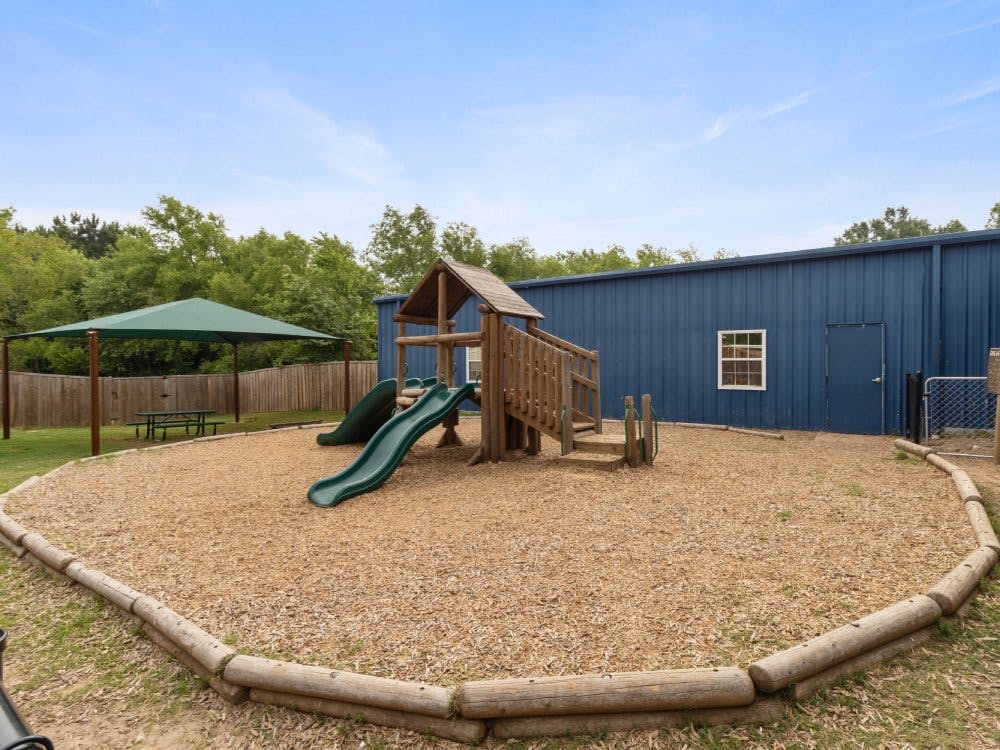 Outdoor playground with wood play structure and green slides, a picnic table under a canopy